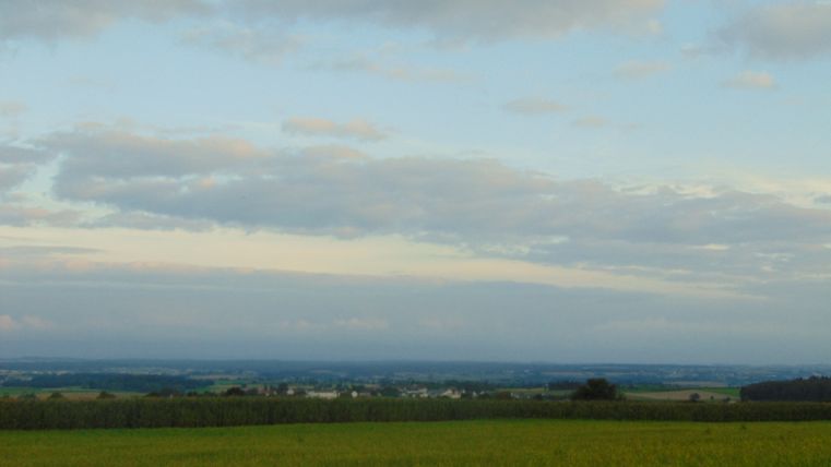 Weite Landschaft mit Feldern und bewölktem Himmel.