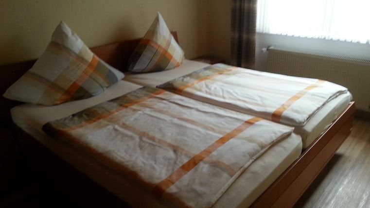 Ein einfaches Schlafzimmer mit einem Doppelbett und zwei Kissen. Die Bettwäsche ist hell und gemustert, und ein Fenster sorgt für Tageslicht.