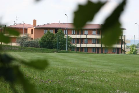 Un bâtiment moderne à plusieurs étages se dresse dans un paysage verdoyant. Entouré de prairies et d'arbres, il semble accueillant et paisible.