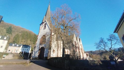 Eine alte Kirche mit einem hohen Turm und klar blauem Himmel. Umgeben von Bäumen und Häusern im Hintergrund.