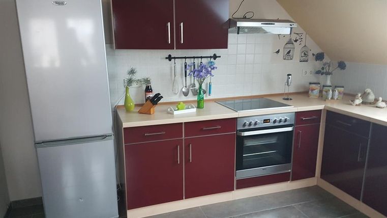 Eine moderne Küche mit rotbraunen Schränken und weißen Fliesen. Der Raum ist mit einem Kühlschrank, einem Herd und Küchenutensilien ausgestattet.