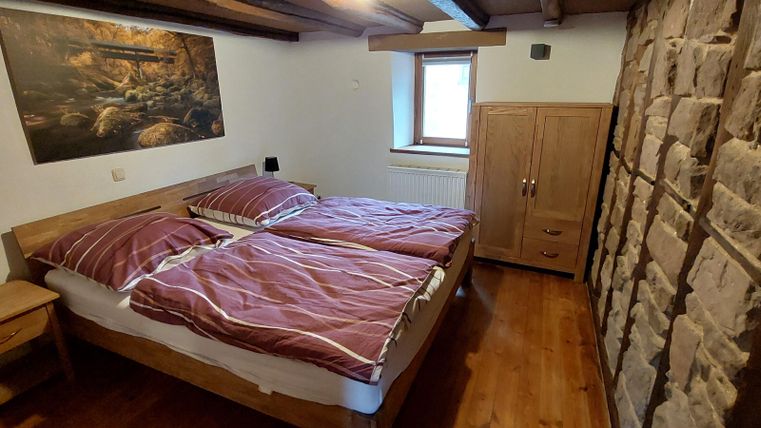 Een gezellig slaapkamer met twee bedden en neutrale decoratie. De muren zijn gedeeltelijk met steen versierd en een groot raam zorgt voor natuurlijk licht.