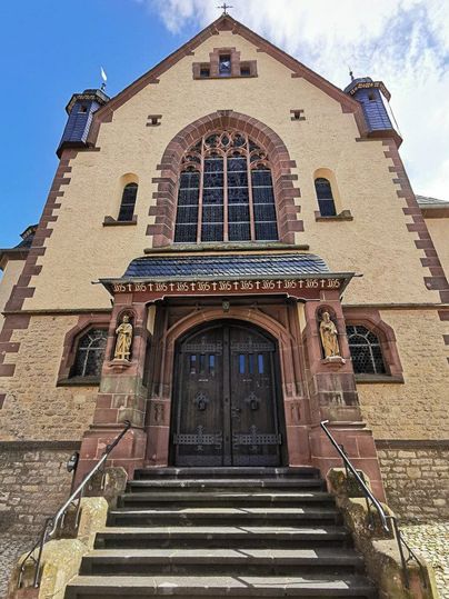 Eingang der Pfarrkirche Maria Königin in Dudeldorf mit Treppe und verzierten Türen.