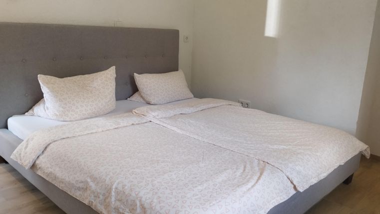 Ein gemütliches Schlafzimmer mit einem großen Bett und hellen Bettwaren. Die Wände sind in neutralen Farben gehalten und es gibt viel natürliches Licht.