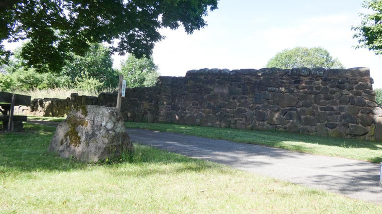 Eine alte Steinmauer in einem grünen Park. Der Weg führt entlang der Mauer unter den Schatten der Bäume.