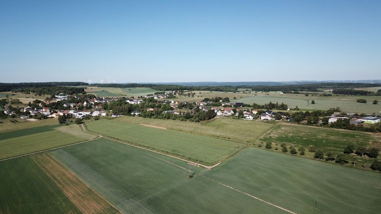 Luchtfoto van Idenheim met velden en windturbines op de achtergrond.