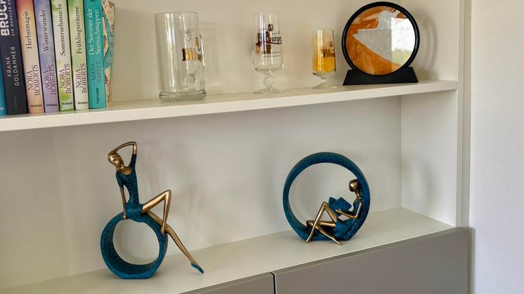 Une étagère moderne avec des sculptures et des verres décoratifs. En arrière-plan, des livres et une horloge créent une atmosphère élégante.