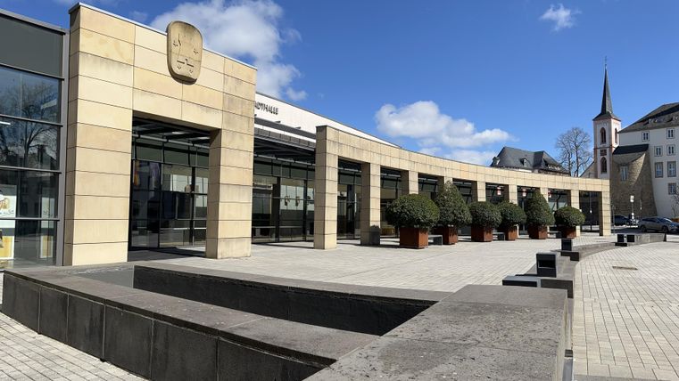 A clear space in front of a modern building with a beautiful plant arrangement. The sun is shining and the sky is blue.