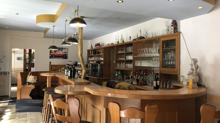 Eine einladende Bar mit Holztheke und einer Auswahl an Getränken. Der Raum ist hell und modern gestaltet.