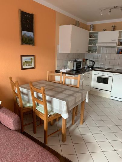 Eine helle Küche mit einem Essbereich und Holzstühlen. Die Wände sind orange und es gibt verschiedene Küchengeräte.