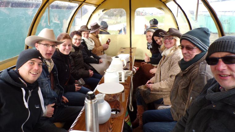 Eine Gruppe von Personen sitzt gemütlich in einem geschützten Raum. Sie trinken etwas und genießen die Gesellschaft.