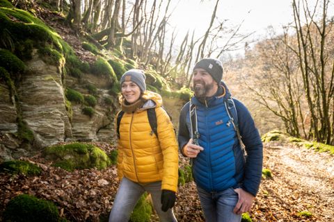 Zwei Wanderer auf einem schönen Waldweg mit grünem Moos und Felsen. Es scheint ein sonniger Tag zu sein und die Natur um sie herum ist lebendig.