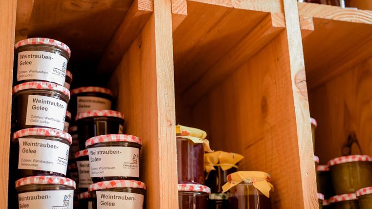 Regale mit verschiedenen Marmeladen und Gelees. Die Gläser haben rot-weiß karierten Deckeln und beschriftete Etiketten.