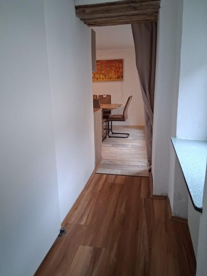 Ein heller Flur mit Holzfußboden, der zu einem gemütlichen Essbereich führt. Im Hintergrund sind Stühle und ein Tisch sichtbar.