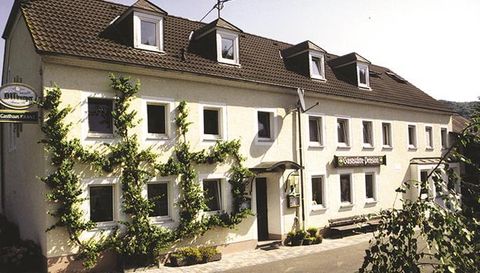 Ein Gebäude mit mehreren Fenstern, das von grünen Pflanzen umgeben ist. Es hat ein einfaches, einladendes Design.