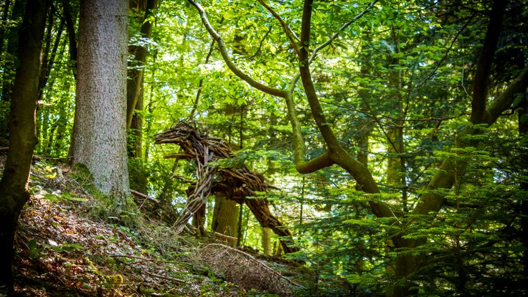 Holzskulptur im Wald, die einem Tier ähnelt.