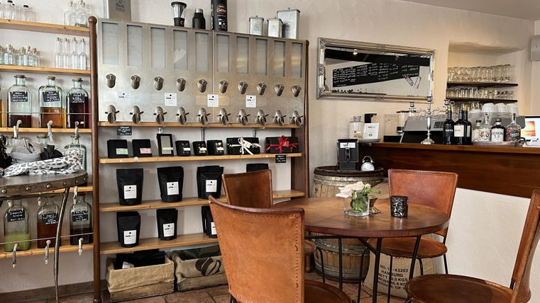 A cozy café with a wooden table and chairs. In the background, shelves with various drinks and accessories can be seen.