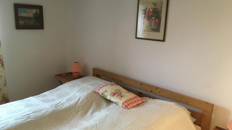 Ein gemütliches Schlafzimmer mit einem großen Bett und einer Decke. An den Wänden hängen Bilder und eine Lampe sorgt für sanftes Licht.