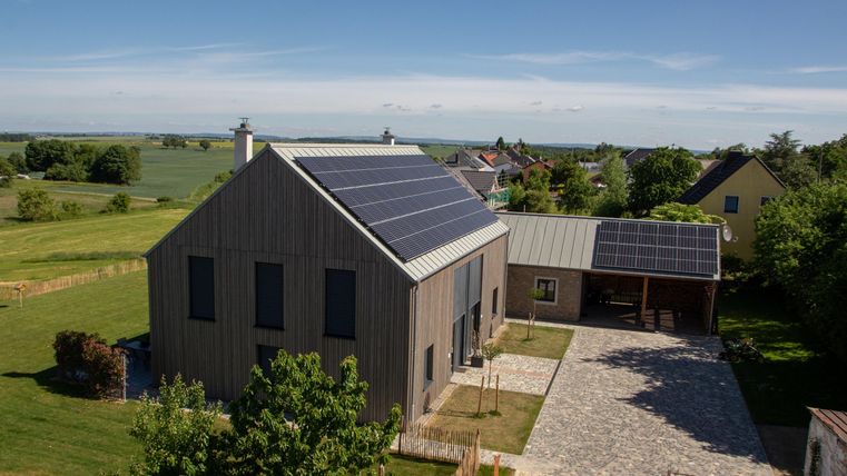 Ein modernes Haus mit Solarpanelen auf dem Dach. Der Garten ist großzügig und die Umgebung ist ländlich und grün.