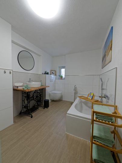 Modernes Badezimmer mit einer freistehenden Badewanne und Holzregal. Helle Wände und ein großer Spiegel sorgen für eine freundliche Atmosphäre.