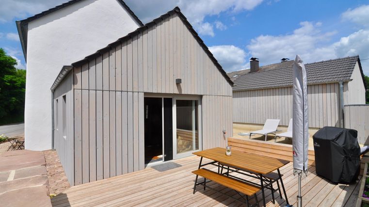 A modern house with wooden cladding and a terrace. On the terrace, there is a table and a grill, perfect for relaxing days outdoors.