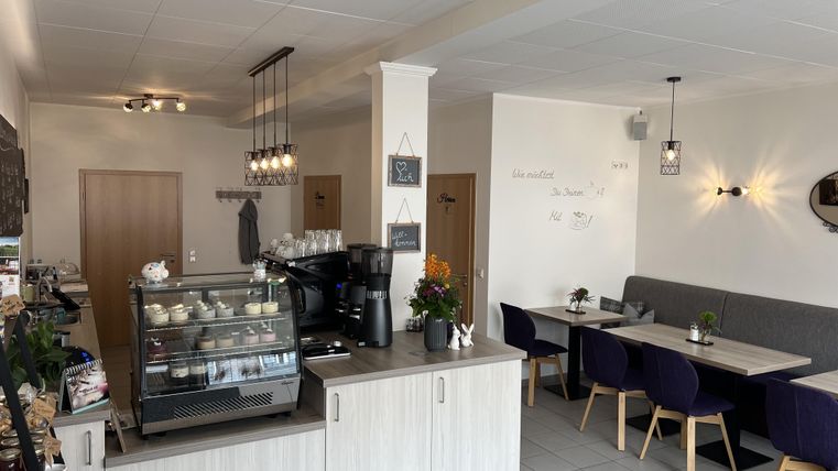 Ein modernes Café mit einer Theke, die Kaffee und Snacks anbietet. Der Raum ist hell und einladend, mit Tischen und Stühlen in gemütlicher Anordnung.