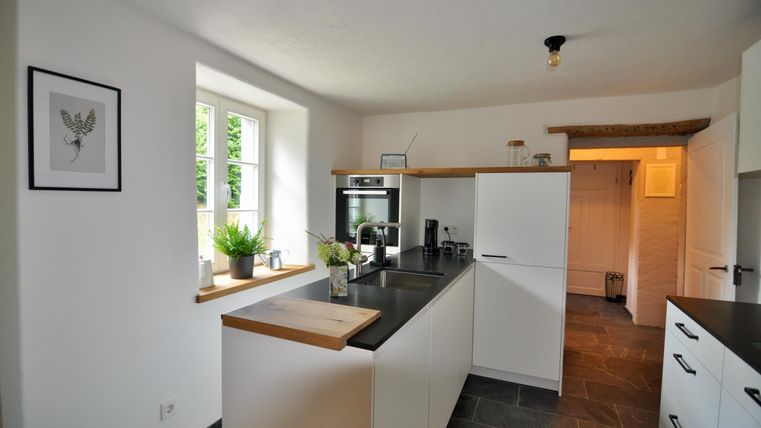 A modern kitchen with white furniture and an elegant countertop. It has large windows that let in a lot of light.