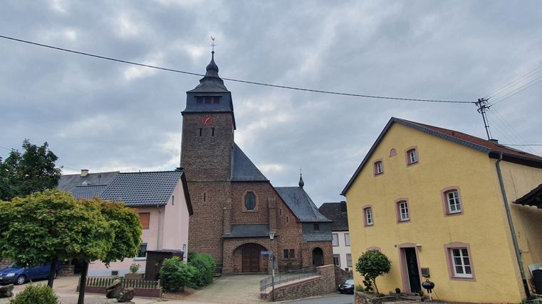 Kirche in Gransdorf mit umliegenden Gebäuden und bewölktem Himmel.