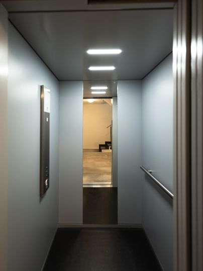 Un ascenseur moderne avec des murs clairs et une vue dégagée sur un escalier. L'éclairage crée une atmosphère accueillante.