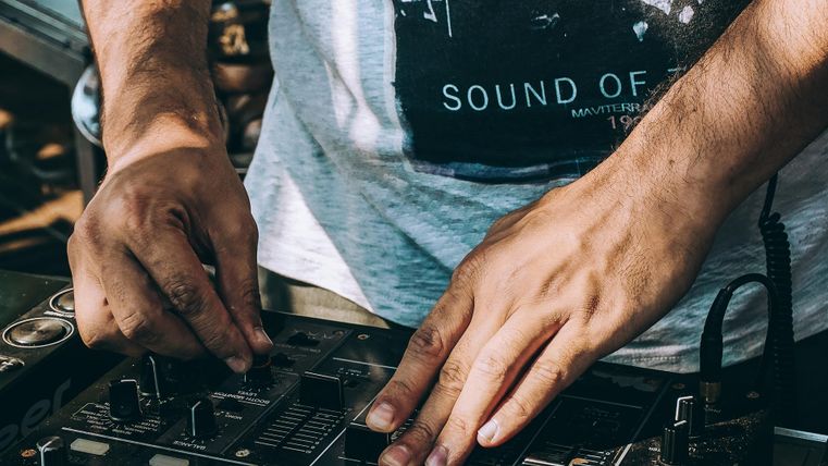 Un DJ qui travaille à une table de mixage. Les mains sont actives et concentrées sur la technologie.