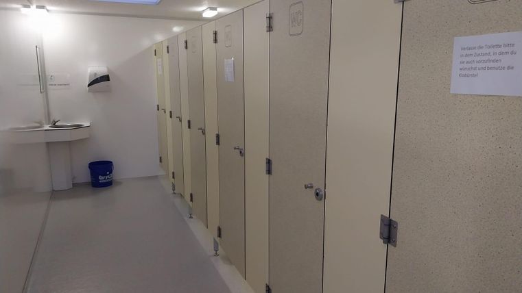 Une zone de toilettes propre avec plusieurs cabines. Un lavabo est accroché au mur et une feuille d'information.