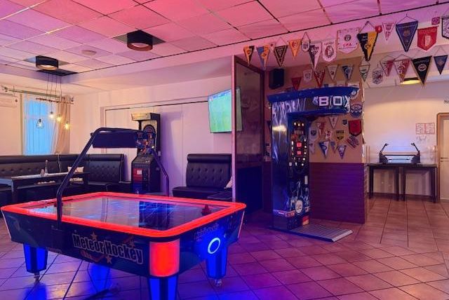 Ein Unterhaltungsraum mit einem Airhockey-Tisch und Spielautomaten. An den Wänden hängen verschiedene Vereinswimpel.