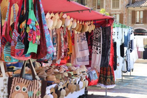 Ein bunter Marktstand mit verschiedenen Stofftaschen und handgemachten Kleidungsstücken. Die Ständer sind unter einem roten Dach aufgestellt und bieten eine Vielzahl an Farben und Designs.