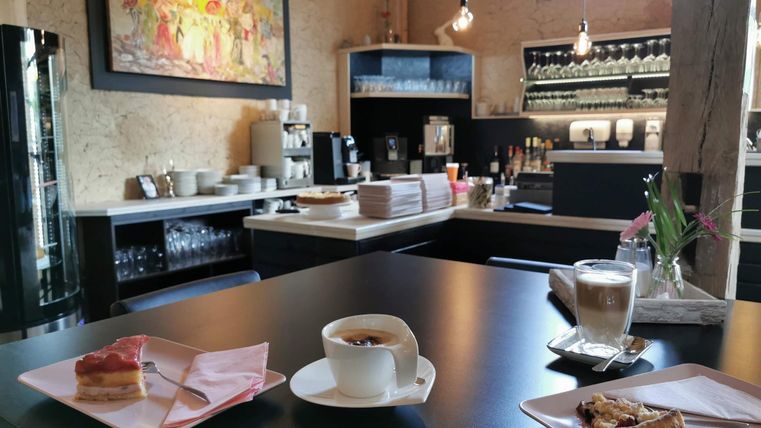 Eine gemütliche Caféecke mit einem modernen Barbereich. Auf dem Tisch stehen Kaffee und Kuchen, umrahmt von einer warmen Atmosphäre.