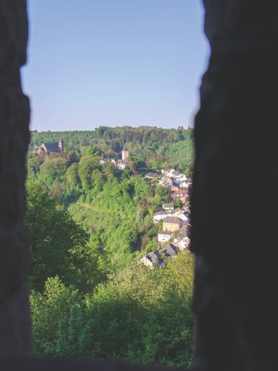Blick auf eine grüne Landschaft mit Kirche und Häusern, eingerahmt von dunklen Silhouetten.
