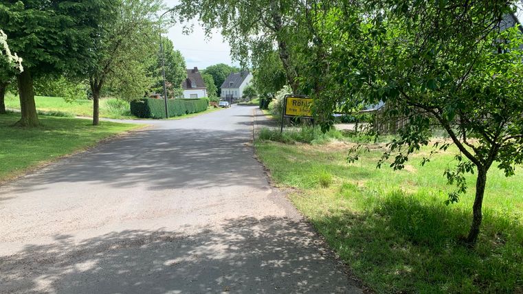 Straße in einem Dorf mit Bäumen und einem Ortsschild mit der Aufschrift 'Röhl'.