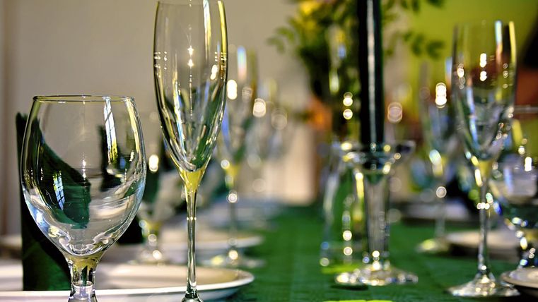 Een feestelijk gedekte tafel met glazen en een zwarte kaars. De decoratie is groen en straalt een uitnodigende sfeer uit.