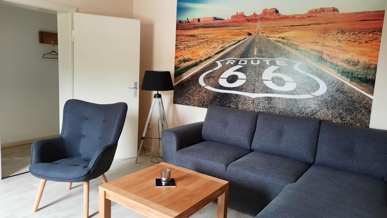 Ein gemütliches Wohnzimmer mit einem grauen Sofa und einem modernen Sessel. An der Wand hängt ein großes Bild von der Route 66 mit einer schönen Landschaft.