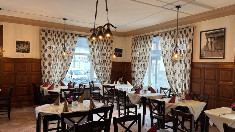 Ein gemütliches Restaurant mit Holzmöbeln und schön gedeckten Tischen. Die Fenster sind mit Vorhängen geschmückt und es gibt eine warme Beleuchtung.