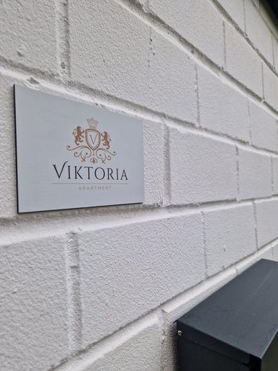 A sign with the inscription "VIKTORIA" on a white wall. Next to it is a gray mailbox.