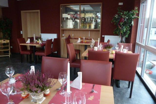 Ein gemütliches Restaurant mit Holz- und Rotakzenten. Die Tische sind hübsch dekoriert und es gibt große Fenster, die viel Licht hereinlassen.