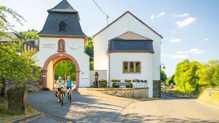 Zwei Radfahrer passieren einen kleinen Torbogen in St. Thomas, umgeben von grüner Landschaft.