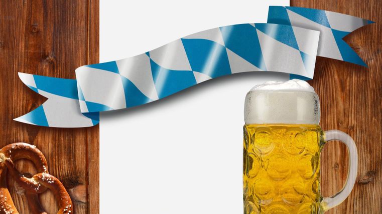 Een bierpul met gouden bier staat naast een pretzel op een houten tafel. Op de achtergrond ligt een leeg vel en een decoratieve blauwe en witte strik.