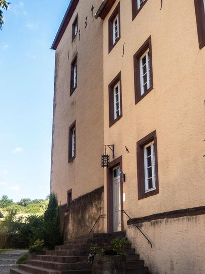 Ein historisches Gebäude mit gelber Fassade und mehreren Fenstern. Der Eingang ist durch eine kleine Treppe zugänglich.