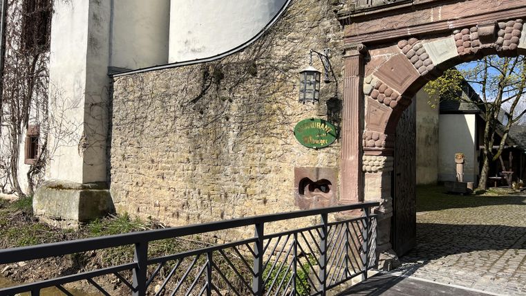 Ein historisches Gebäude mit einer schönen Steinfassade und einem romantischen Tor. Eine Brücke führt über einen kleinen Wasserlauf zum Eingang.