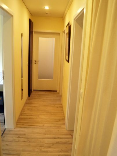 Ein heller Flur mit gelben Wänden und einem modernen Holzfußboden. Auf der linken Seite befinden sich mehrere Türen.