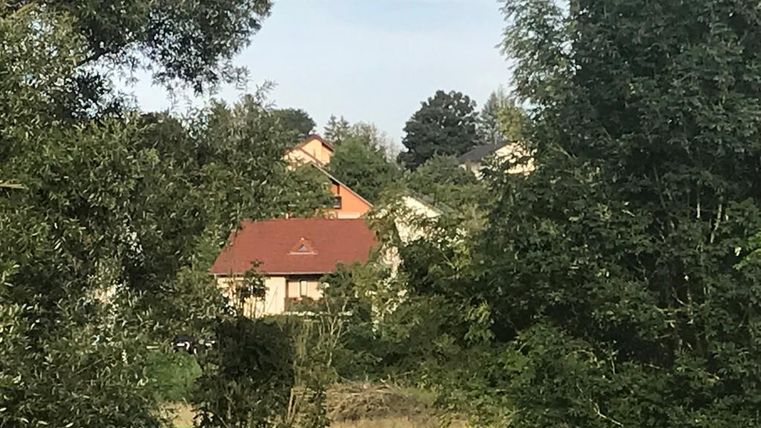 Een blik op een rustig woongebouw, omgeven door bomen en groen. De lucht is lichtbewolkt.