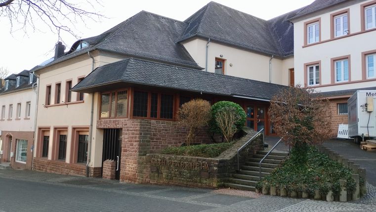 Een modern gebouw met een steile dak en grote ramen. Voor de ingang zijn er trappen en decoratieve planten.