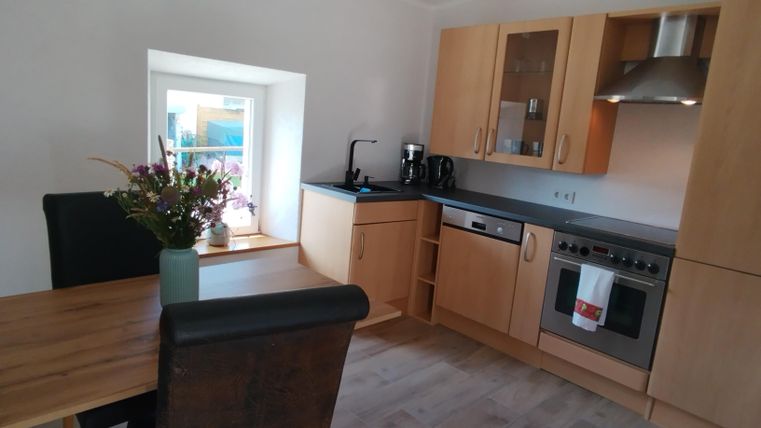 Eine moderne Küche mit hellen Holzmöbeln und einer großen Fensterbank. Auf dem Tisch steht eine Vase mit frischen Blumen, und die Küchengeräte sind gut sichtbar.