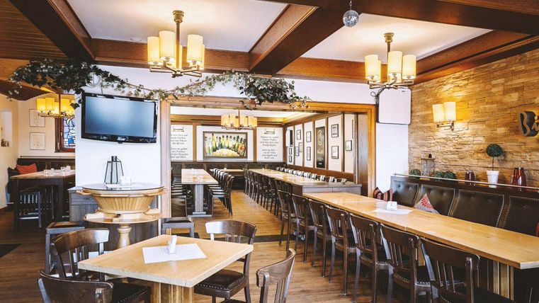 Ein gemütliches Restaurant mit Holztischen und Stühlen. Wände sind mit Bildern geschmückt und es gibt eine Bar im Hintergrund.